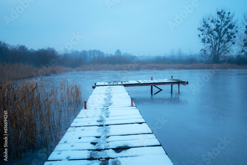Snow on a wooden pier on the lake shore, view on a foggy December day © darekb22