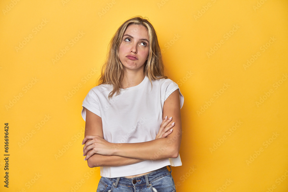 Young blonde Caucasian woman in a white t-shirt on a yellow studio background, tired of a repetitive task. Young blonde Caucasian woman in a white t-shirt on a yellow studio background, tired of a repetitive task.