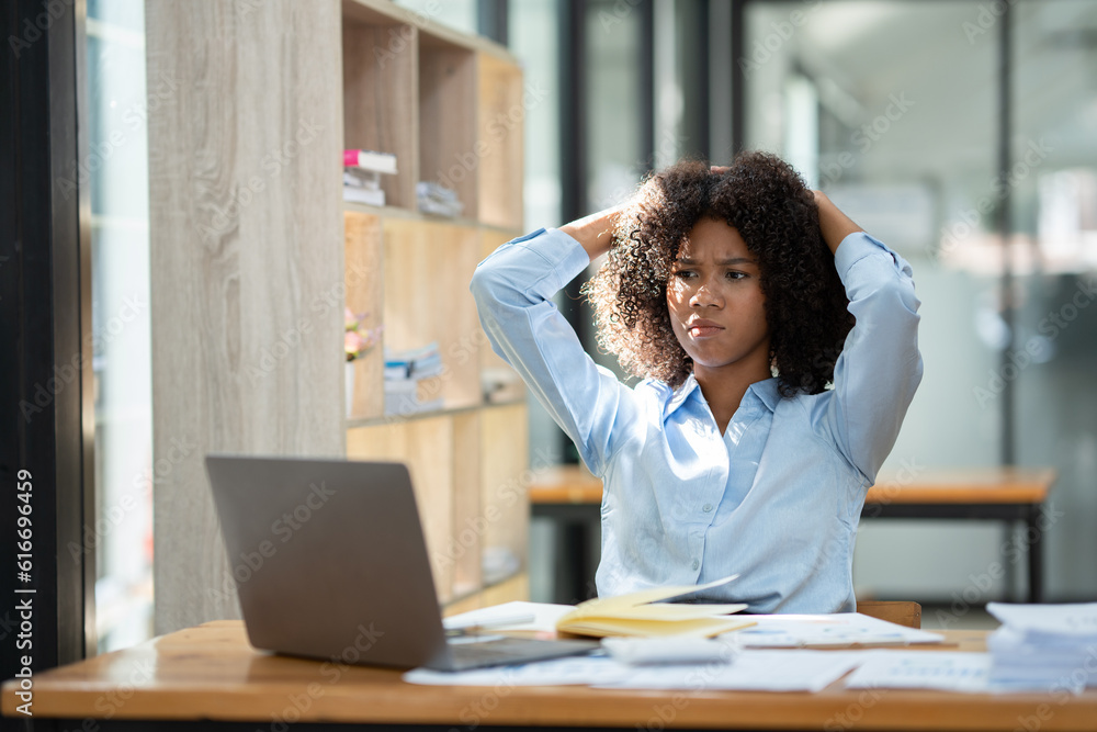Young American businesswoman working on the laptop with documents and stressing at work from working on financial documents in office Overworked woman concept. Young American businesswoman working on the laptop with documents and stressing at work from working on financial documents in office Overworked woman concept.