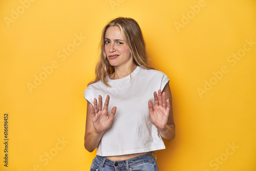 Billede på lærred Young blonde Caucasian woman in a white t-shirt on a yellow studio background, rejecting someone showing a gesture of disgust
