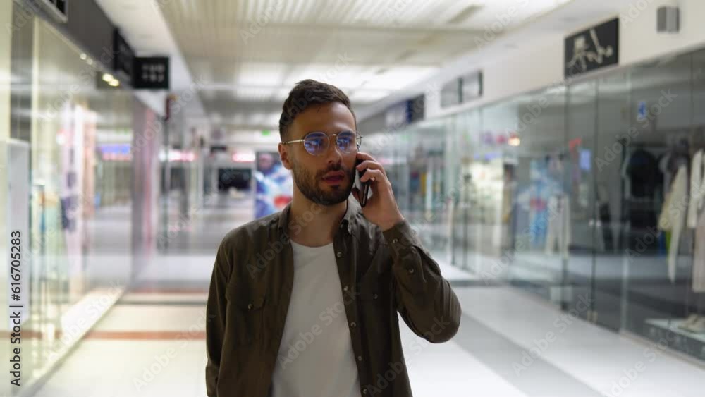 Handsome young man talking on a mobile phone and smiling while walking in mall Handsome young man talking on a mobile phone and smiling while walking in mall