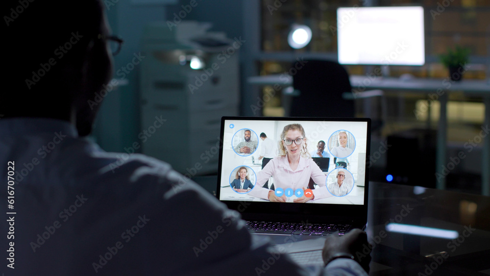 Back view of African-American businessman having video conference late in office Back view of African-American businessman having video conference late in office