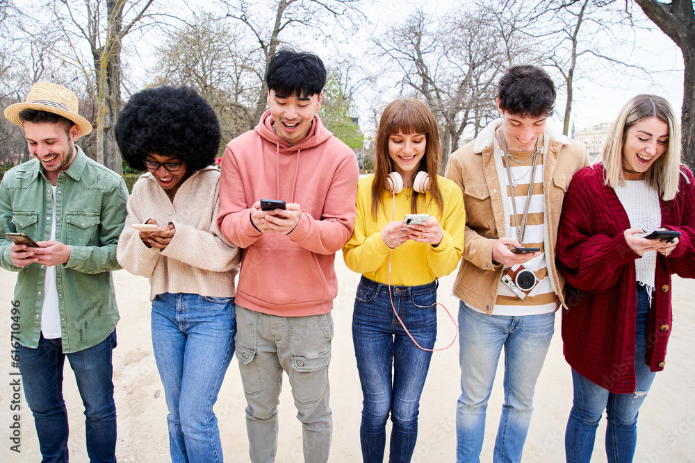 Group of multiracial young cheerful students watching their mobiles. Communication with friends and check social media with their smart phones. People, technology addiction and millennial generation