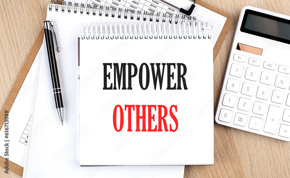 EMPOWER OTHERS is written in white notepad near a calculator, clipboard and pen. Business concept EMPOWER OTHERS is written in white notepad near a calculator, clipboard and pen. Business concept