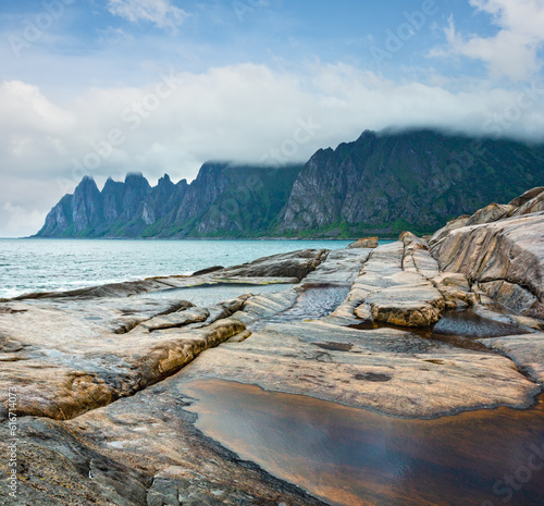 Stony beach with tidal baths at Ersfjord, Senja, Norway. Summer polar day night coast. The dragon teeth rock in far. photo