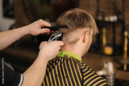 Back view of barber using trimmer to make haircut for customer