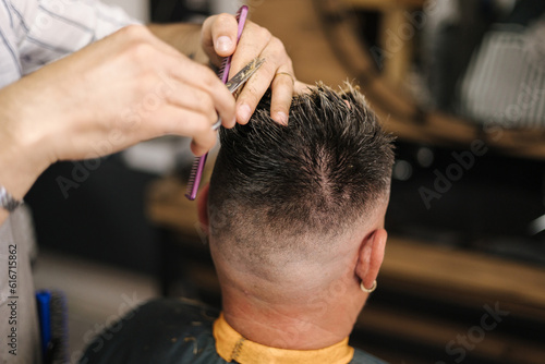 Back view of barber using scissors and making hairstyle. Modern barbershop