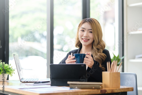 Millennial businesswoman sitting at her workplace with financial document and smiling to camera.