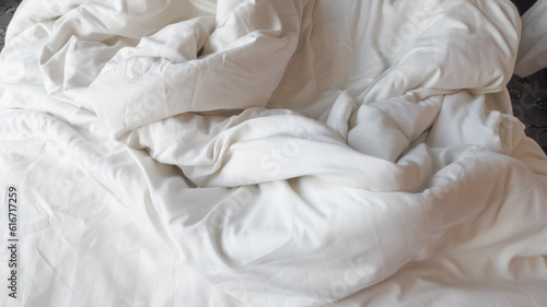 Selective focus of disheveled and wrinkled white soft linen blanket on the bed.
