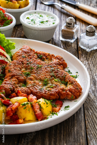 Breaded fried pork chop with fresh vegetable salad and potatoes on wooden table 