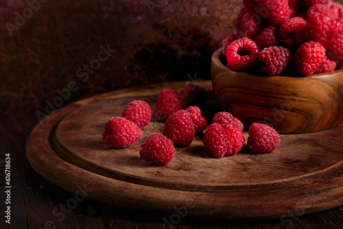 Red raspberries in a wooden bowl on wooden board background.