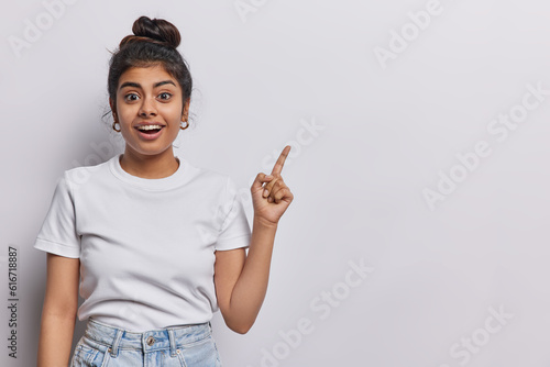 Tela Horizontal shot of pretty surprised cheerful young woman pointing to empty copy