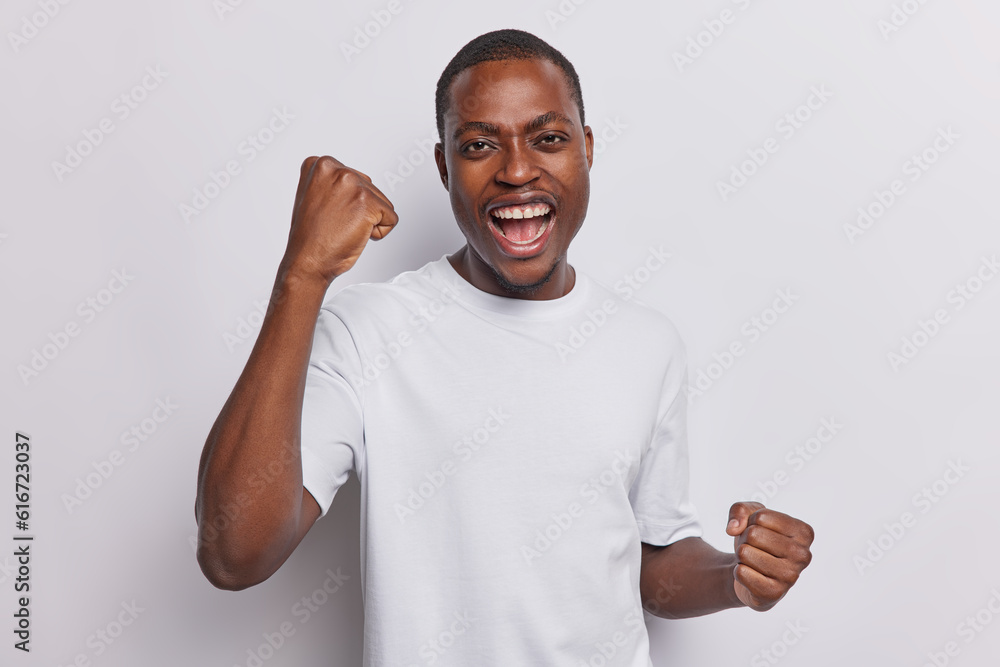 Man with dark skin filled with emotion exudes jubilation celebrates moment of triumph with clenched fists and open mouthed exclamation passionately supports favorite team shows victorious enthusiasm. Man with dark skin filled with emotion exudes jubilation celebrates moment of triumph with clenched fists and open mouthed exclamation passionately supports favorite team shows victorious enthusiasm.