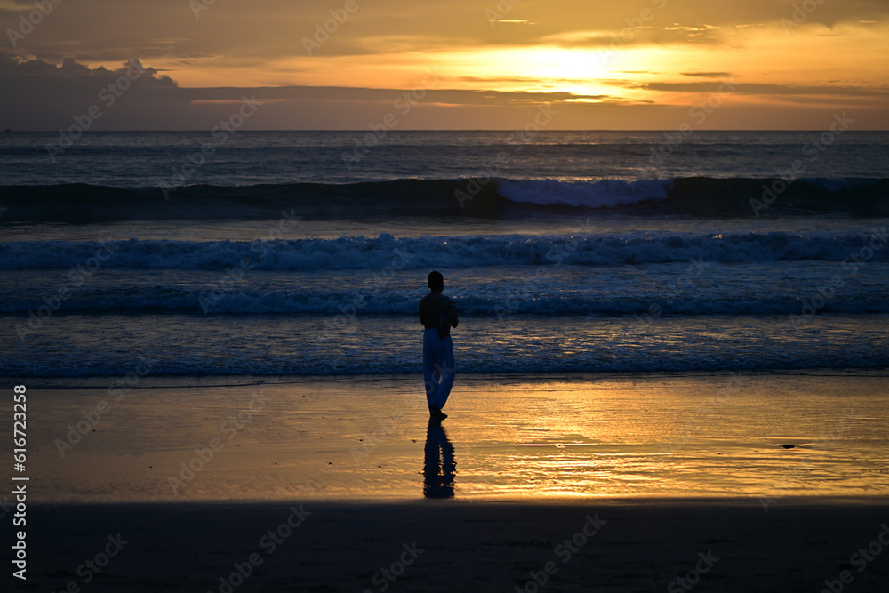 Fototapeta premium A man walks at the beach of Phuket-Thailand in the sunset while he looks at his smartphone.