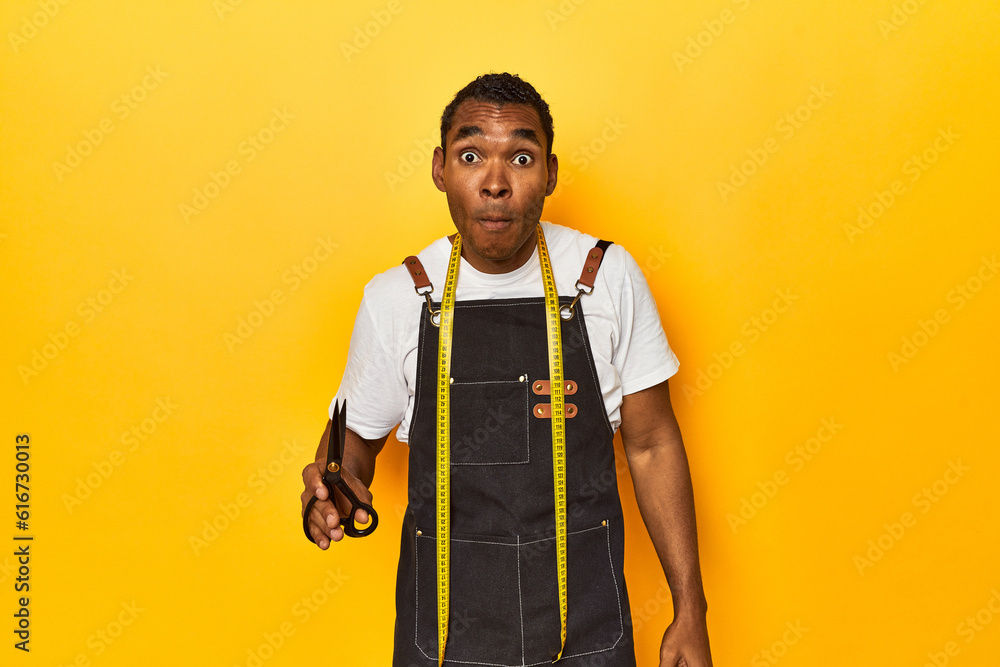 African American tailor with tools, yellow studio, shrugs shoulders and open eyes confused. African American tailor with tools, yellow studio, shrugs shoulders and open eyes confused.