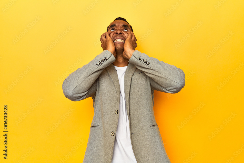 African American man in casual blazer, yellow studio, whining and crying disconsolately. African American man in casual blazer, yellow studio, whining and crying disconsolately.