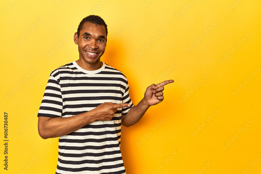 African American man in striped t-shirt, yellow studio, excited pointing with forefingers away. African American man in striped t-shirt, yellow studio, excited pointing with forefingers away.