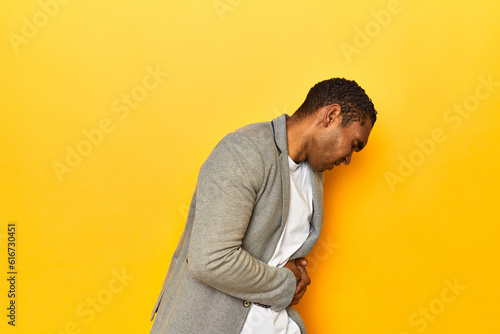 African American man in casual blazer, yellow studio, having a liver pain, stomach ache. © Asier