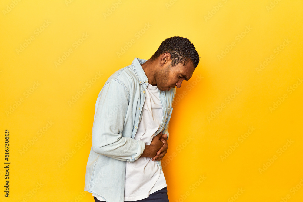 African American man in blue shirt, yellow studio, having a liver pain, stomach ache. African American man in blue shirt, yellow studio, having a liver pain, stomach ache.
