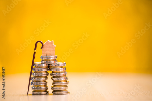 Home model put on the stack gold coin with growing interest and walking cane on the yellow background in the office, Saving money for retirement and planning in the future concept.