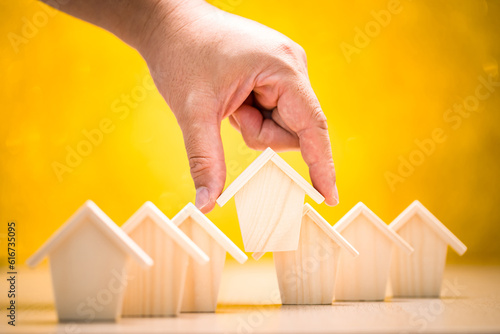 Businessman hand hold for select a home model on the yellow background  in the office, Loan for real estate or saving money for buy a new house to family in the future concept.