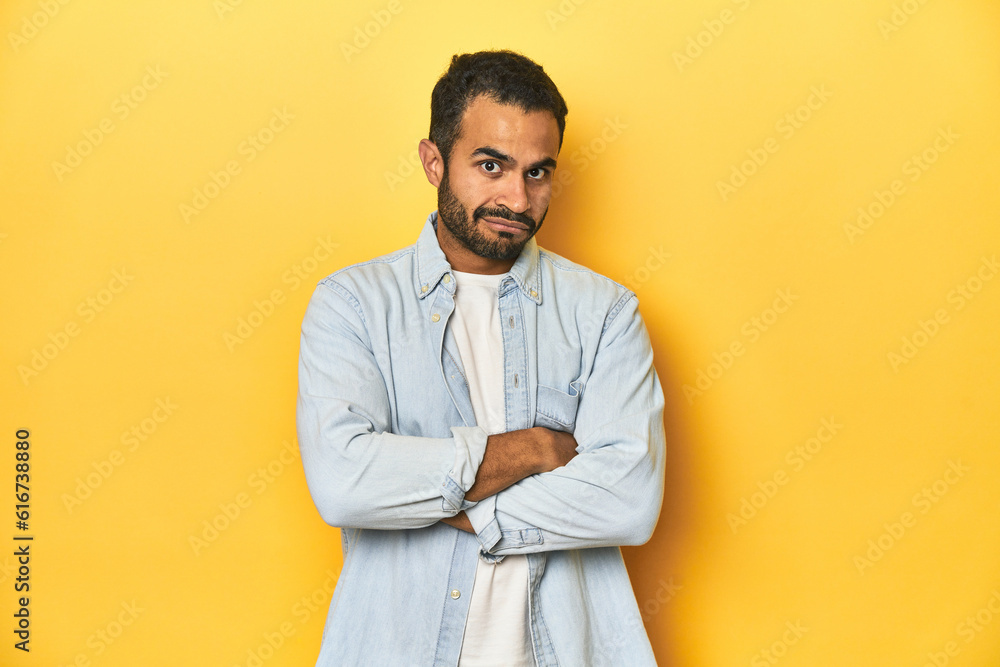 Fototapeta premium Casual young Latino man against a vibrant yellow studio background, suspicious, uncertain, examining you.