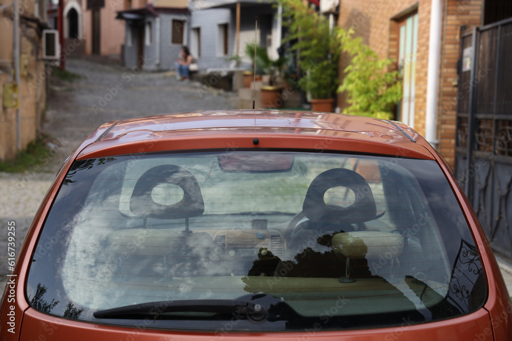 Back window of orange, brown car parked on the street near houses, rear view. Mock-up for sticker or decals. rear view. Kutaisi, Georgia. Transparent glass with reflection. empty vehicle.