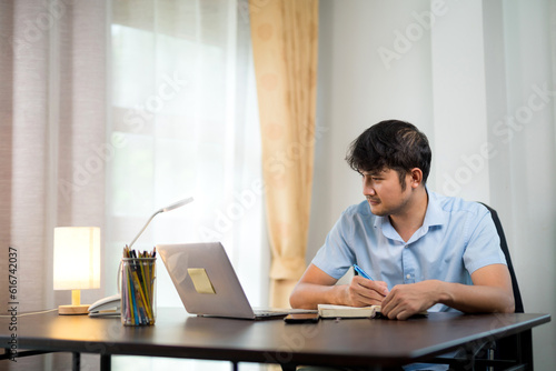 Asian handsome man taking notes while learning online video conference at home.