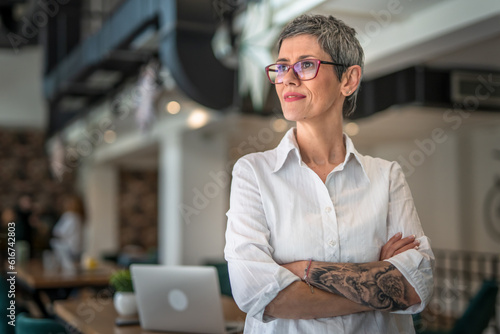 One senior woman with tattoo on left hand standing at cafe  with crossed hands, modern lifestyle portrait concept 