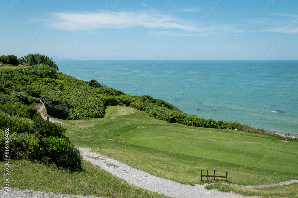 Campo de golfe junto ao mar com uma trilha em gravilha a meio e algumas árvores num dia ensolarado