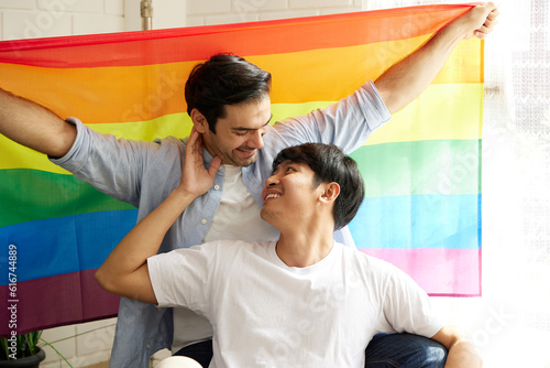 young gay couple with rainbow flag(LGBT) smiling and looking each other