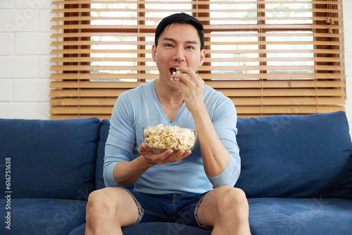 young handsome man watching movies and eating popcorn in a living room #616751638
