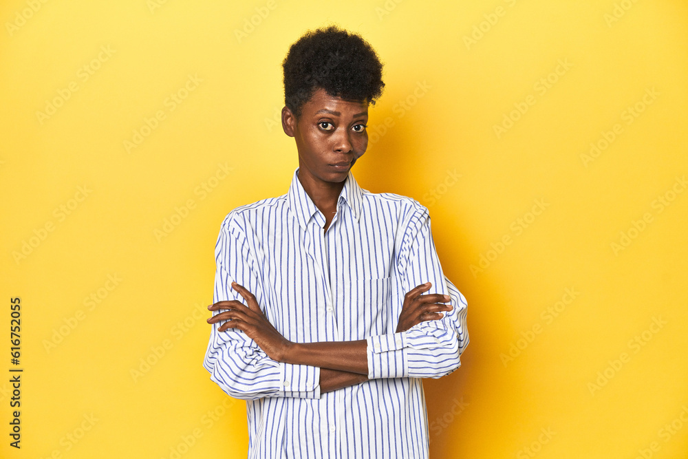 African businesswoman, blue striped shirt, yellow backdrop, suspicious, uncertain, examining you. African businesswoman, blue striped shirt, yellow backdrop, suspicious, uncertain, examining you.