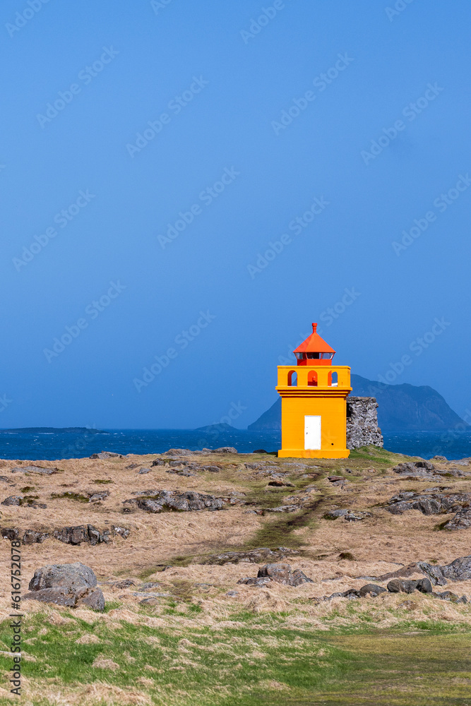 A orange red lighthouse at the coast of iceland in summer on a really sunny day
