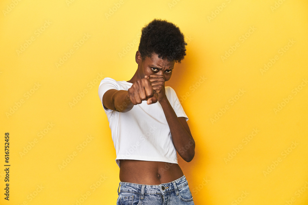 African woman, white tee, short hair, yellow studio, throwing a punch, anger, fighting due to an argument, boxing. African woman, white tee, short hair, yellow studio, throwing a punch, anger, fighting due to an argument, boxing.