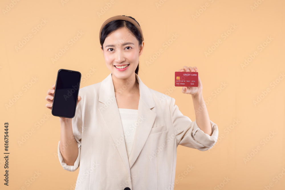 portrait of happy successful confident young asian business woman wearing white jacket holding smartphone and credit card standing over beige background. shopping concept. portrait of happy successful confident young asian business woman wearing white jacket holding smartphone and credit card standing over beige background. shopping concept.