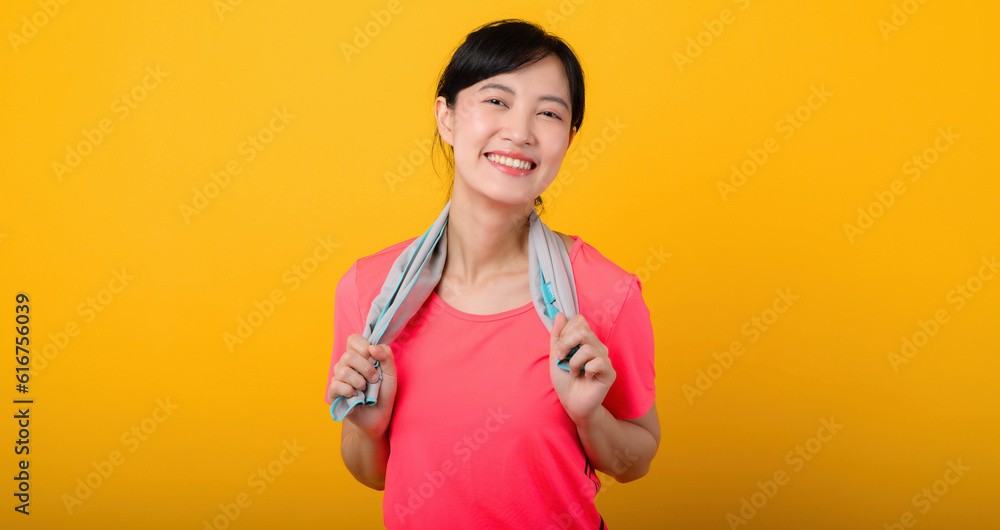 Portrait young asian sports fitness woman happy smile wearing pink sportswear and face towel doing exercise training workout against yellow studio background. wellbeing and healthy lifestyle concept.