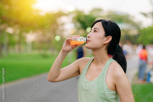 Wallpaper Mural Female jogger. Fit young Asian woman with green sportswear drinking organic orange juice after running and enjoying a healthy outdoor. Fitness runner girl in public park. Wellness being concept Torontodigital.ca
