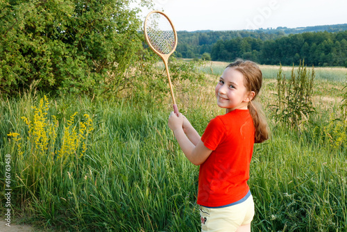 cute little girl with a smile holding a badminton racket in the countryside