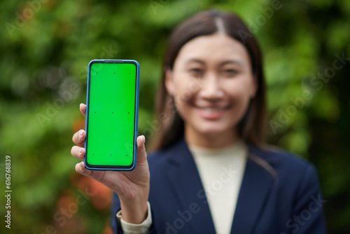 Smiling businesswoman showing smartphone with green screeb when standing outdoors photo