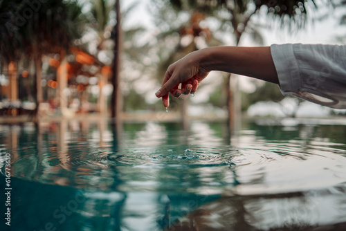 An elegant woman s hand touches the surface of the turquoise water  creating ripples  symbolizing the connection between humans and nature.