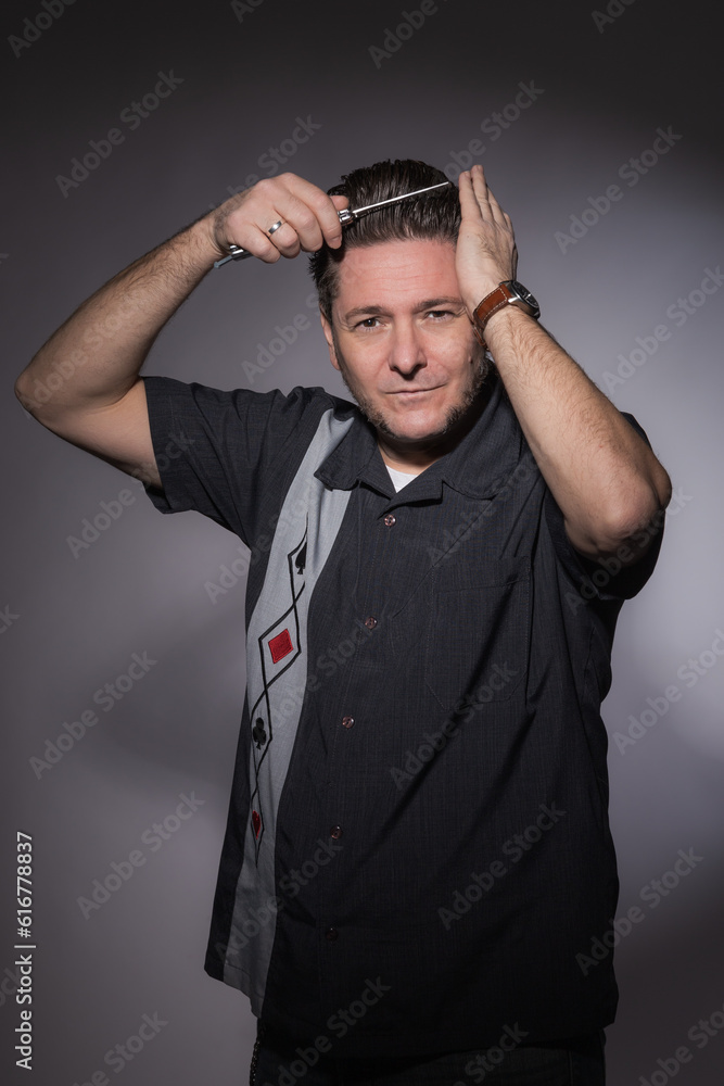 Vertical studio portrait of a 40 years old man in rockabilly style combing his hair with a steel folding butterfly comb Vertical studio portrait of a 40 years old man in rockabilly style combing his hair with a steel folding butterfly comb