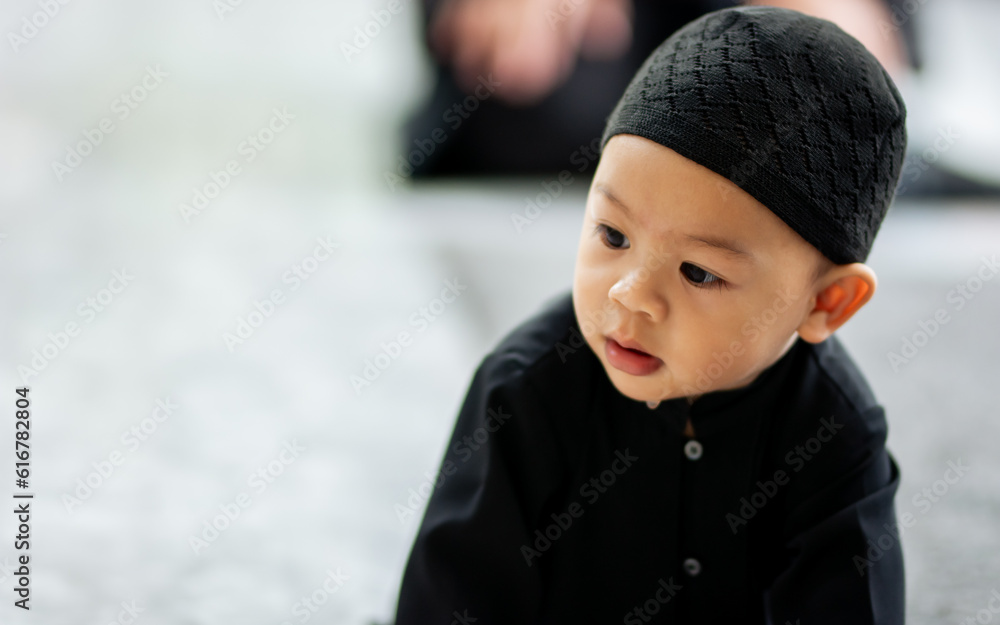 Portrait cute innocent little baby muslim boy wearing traditional clothes, sitting on floor in living room at home, playing alone with copy space. Education, Kid, Religious Concept. Portrait cute innocent little baby muslim boy wearing traditional clothes, sitting on floor in living room at home, playing alone with copy space. Education, Kid, Religious Concept.