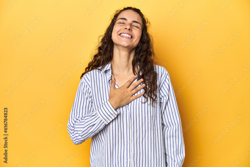 Young Caucasian woman, yellow studio background, laughs out loudly keeping hand on chest. Young Caucasian woman, yellow studio background, laughs out loudly keeping hand on chest.