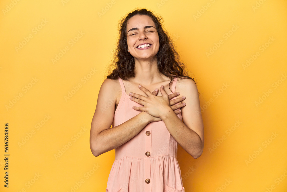 Obraz premium Young Caucasian woman, yellow studio background, laughing keeping hands on heart, concept of happiness.