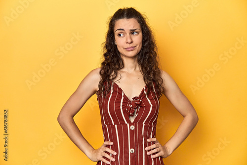 Young Caucasian woman, yellow studio background, confused, feels doubtful and unsure.