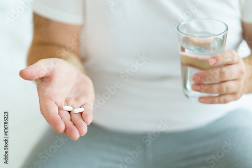 Unwell caucasian man got a sickness, oversize fat man taking a pills and drinking water in a drinking glass after wake up in morning.