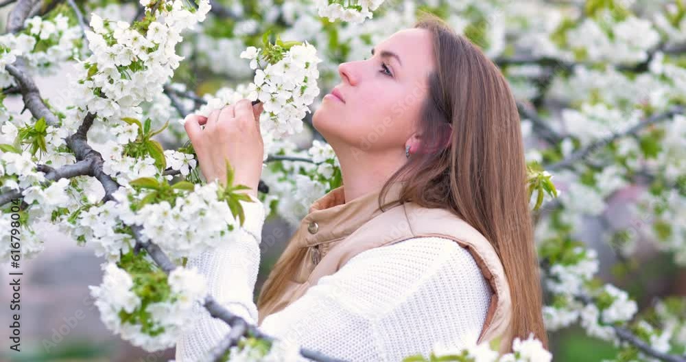 Woman holding a branch of a flowering tree in her hands and sniffing flowers Woman holding a branch of a flowering tree in her hands and sniffing flowers