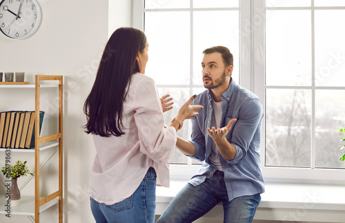 Annoyed young family couple arguing emotionally, blaming each other. Stressed irritated woman and man shouting at each other having serious relations communication problems. Couple quarreling at home photo