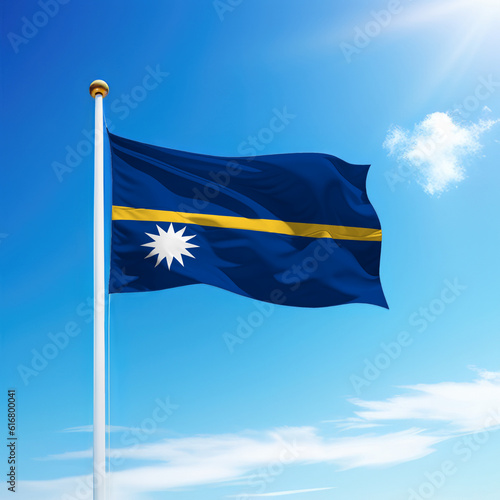 Waving flag of Nauru on flagpole with sky background.